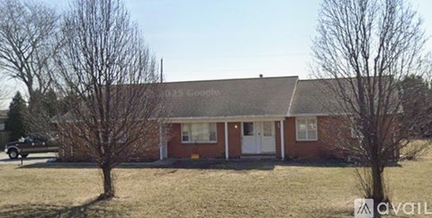 A red brick house with a white door and a tree in front.