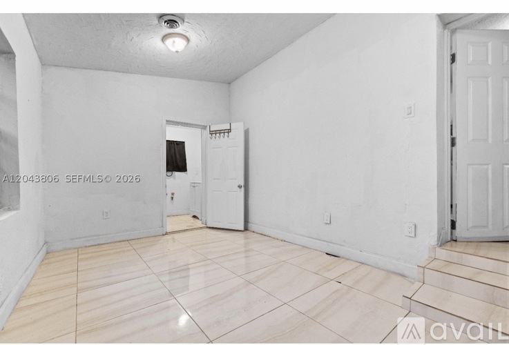 A room with white walls and a wooden floor with a door on the right side.