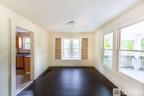 A spacious room with a large window and wooden flooring.