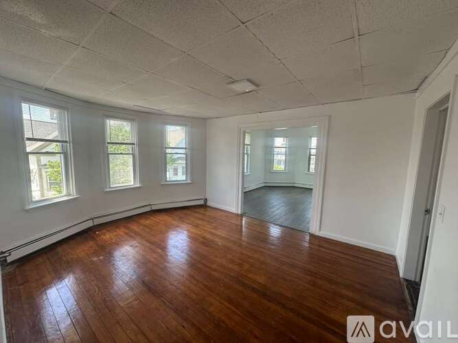 A room with wooden floors and white walls, with windows on the left side.