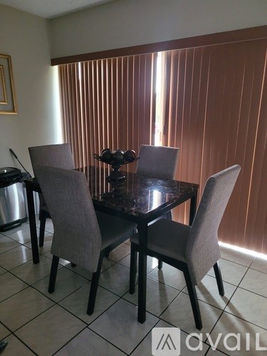 A dining table with four chairs and a bowl of fruit on top.