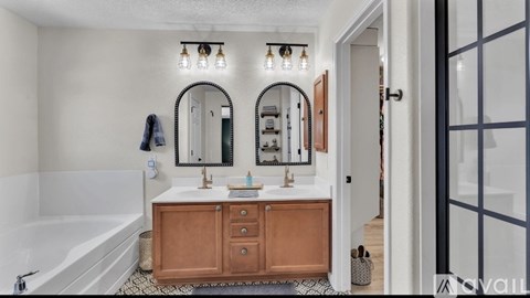 A bathroom with a white tub, a sink with a wooden cabinet and a mirror above it.