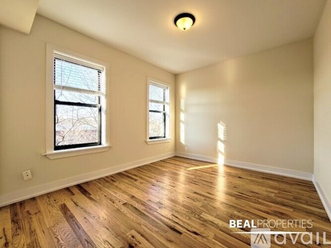 A room with wooden flooring and two windows.