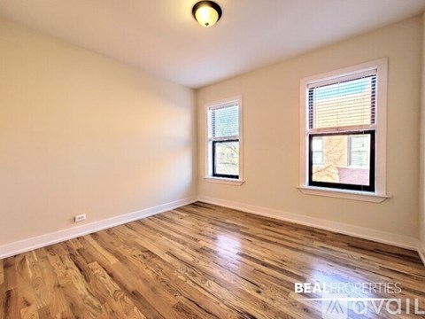 A room with wooden flooring and two windows.