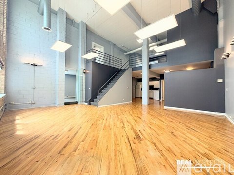 A spacious room with wooden floors and a staircase.