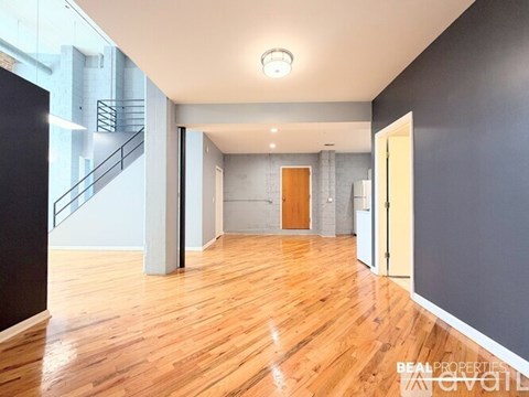 A spacious room with wooden floors and a staircase in the background.