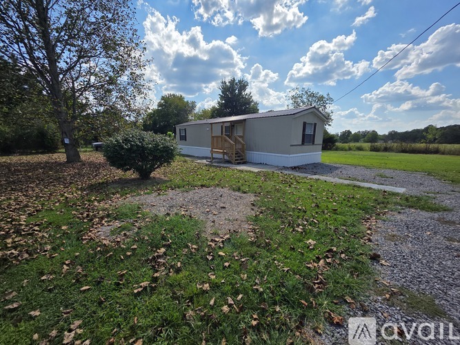 A mobile home sits in a grassy field with a gravel path leading to it.
