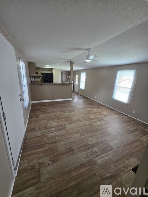 A room with wooden flooring and a kitchen area in the background.