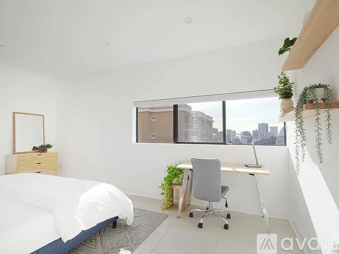 A bedroom with a bed, desk, chair, and a window overlooking a cityscape.