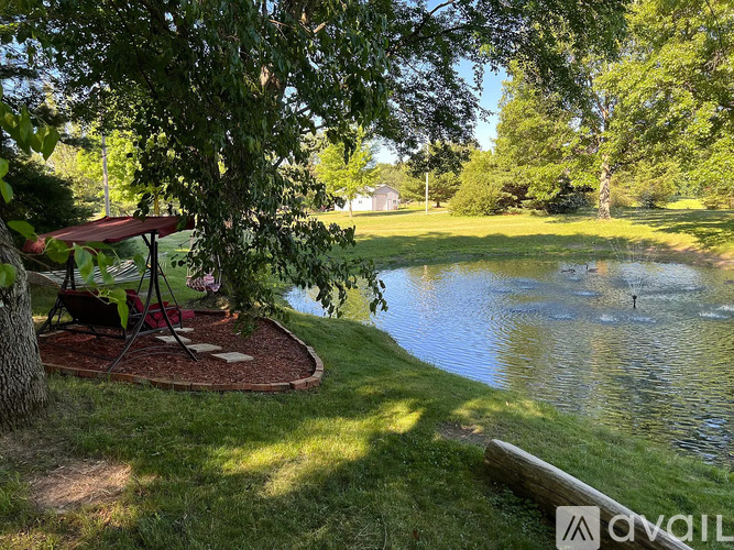 A tranquil scene with a pond, a gazebo, and a tree in the foreground.