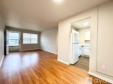 A room with wooden floors and a kitchen area in the background.