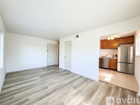 A spacious room with wooden flooring and a kitchen area in the background.
