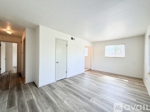 A spacious room with wooden flooring and white walls.