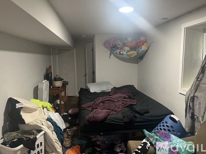 A messy bedroom with a bed, clothes, and a fan.