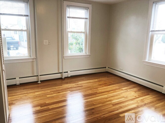 A room with wooden floors and three windows.