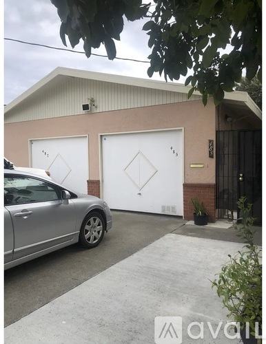 A silver car is parked in front of a house with two white garage doors.