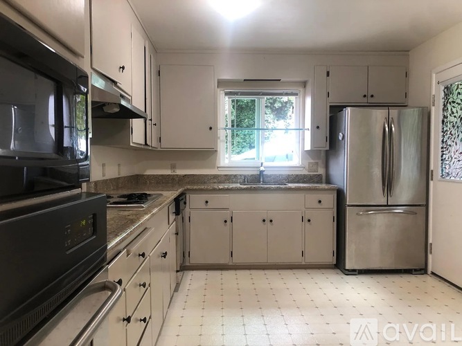 A kitchen with a black microwave, white cabinets, and a stainless steel refrigerator.