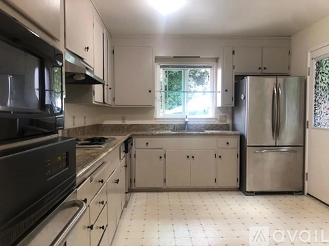 A kitchen with a black microwave, white cabinets, and a stainless steel refrigerator.