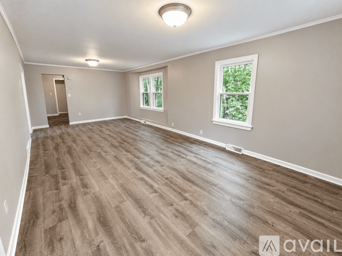A spacious room with wooden flooring and a window with a view of greenery outside.