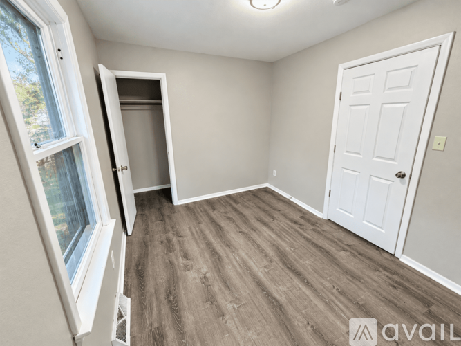 A room with a white door and a window with a view of trees.