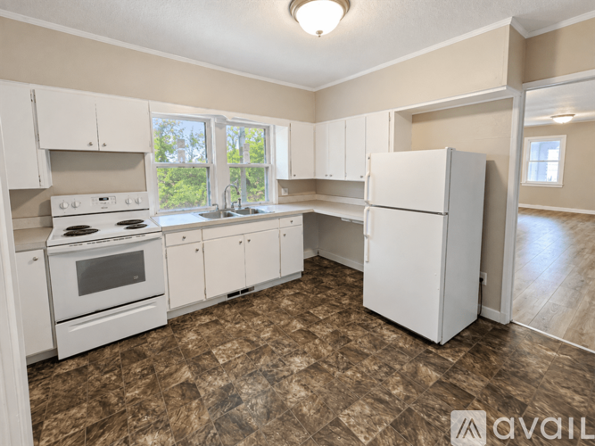 A kitchen with white appliances and brown tiled flooring.