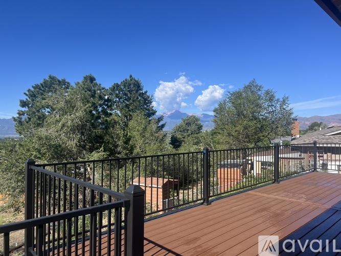 A balcony with a black railing and a wooden floor overlooks a mountainous landscape.