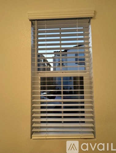 A window with white blinds partially open.
