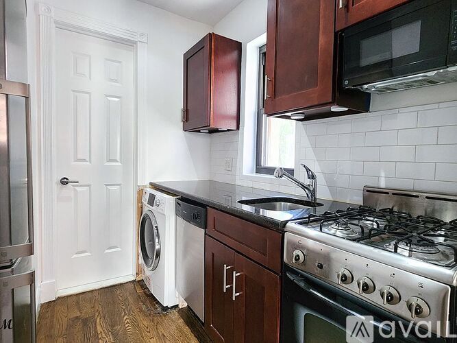 A kitchen with a white door, a washing machine, a stove, and a microwave.