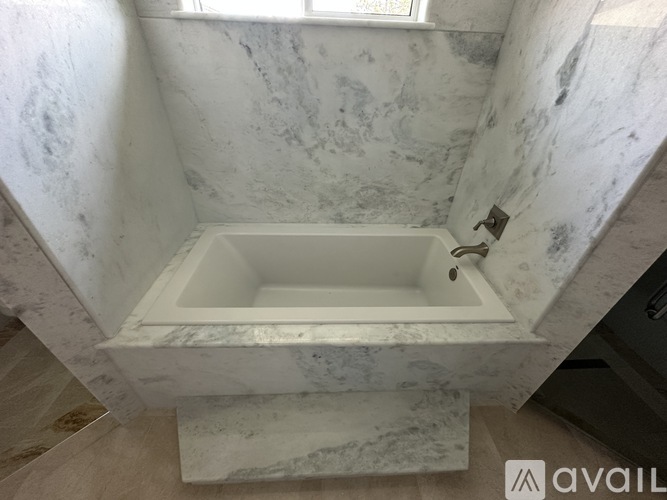 A white marble bathroom with a tub and a window.