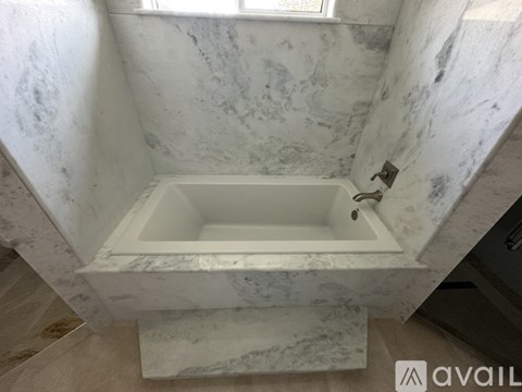 A white marble bathroom with a tub and a window.
