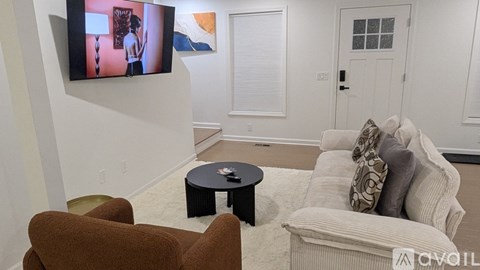 A living room with a brown chair, a white couch, and a television mounted on the wall.