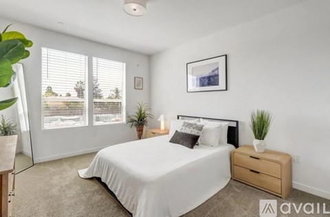 A bedroom with a large bed, a nightstand, and a window with blinds.