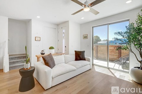A living room with a white couch, a ceiling fan, and a view of the backyard through the sliding glass door.