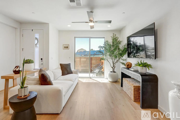 A living room with a white couch, wooden floor, and a flat screen TV mounted on the wall.
