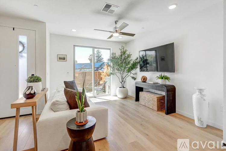 A living room with a white couch, a wooden side table, a TV, and a plant.