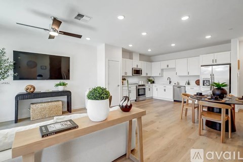 A modern kitchen with a dining table and chairs, a plant on the table, and a fan on the ceiling.