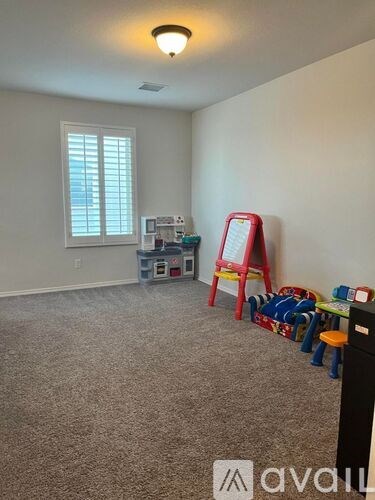 A room with a carpeted floor, a window with blinds, a red chair, a whiteboard, and some toys.