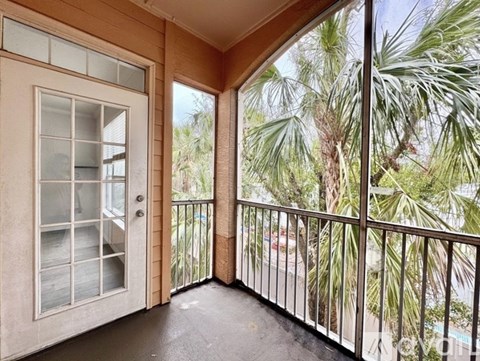 A balcony with a door and a view of a pool and trees.