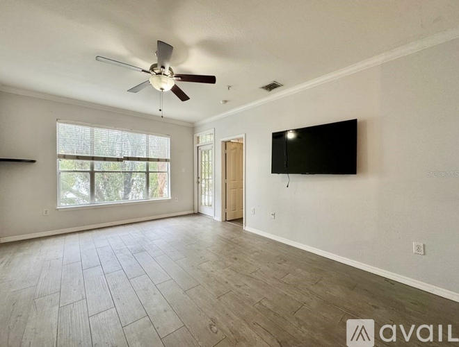 A spacious living room with a ceiling fan and a flat screen TV mounted on the wall.