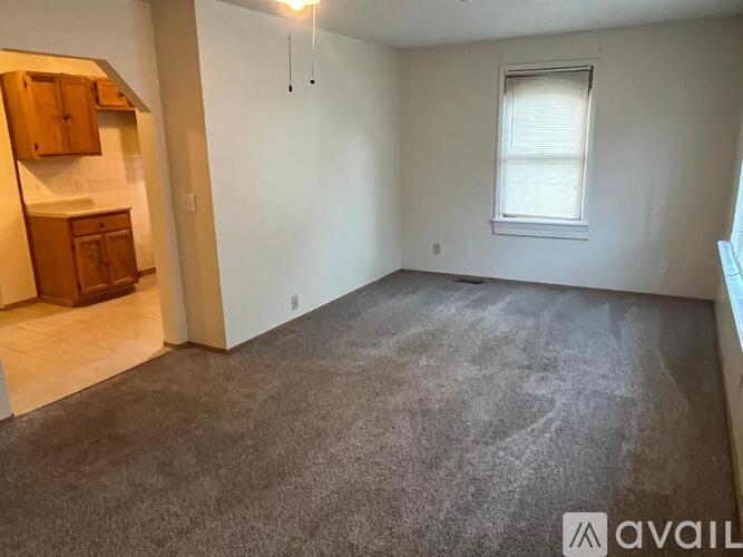 A room with a carpeted floor, a window with blinds, and a wooden cabinet.