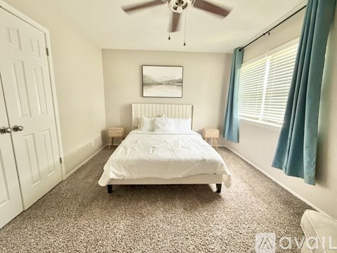 A bedroom with a white bed and a ceiling fan.