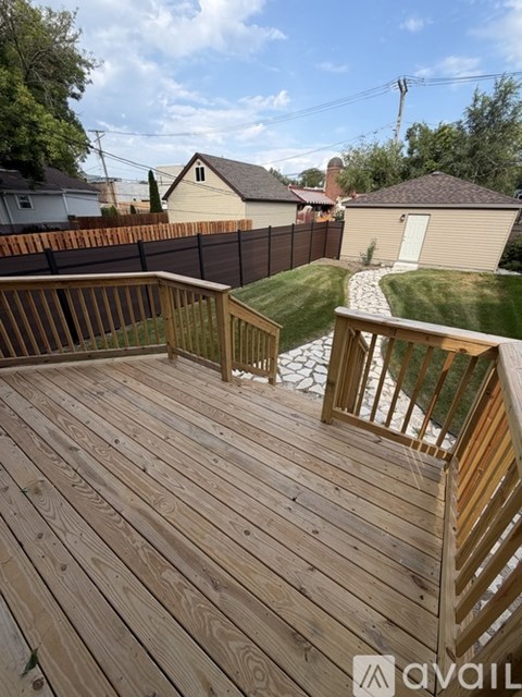A wooden deck with a railing and a stone pathway leading to a house.