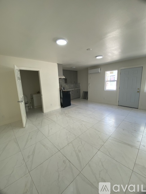 A spacious room with white tiled flooring and a large open doorway leading to another room.