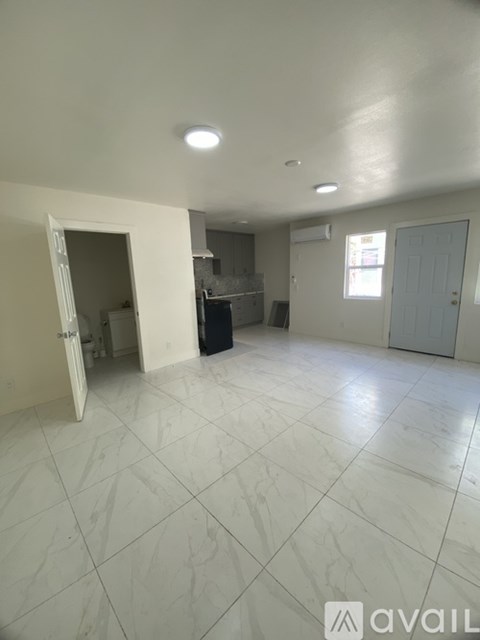 A spacious room with white tiled flooring and a large open doorway leading to another room.