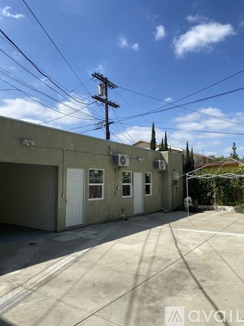 A building with a grey facade and a white door is surrounded by a concrete driveway.