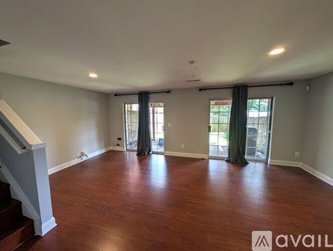 A spacious room with wooden floors and a staircase on the left side.