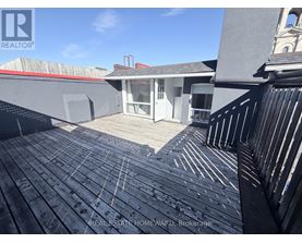 A wooden deck with a railing and a building in the background.