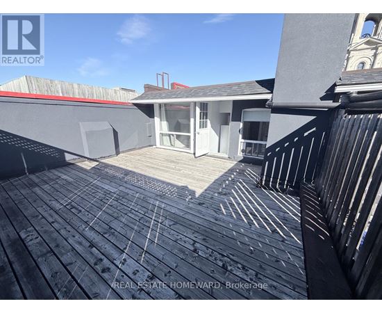 A wooden deck with a railing and a building in the background.