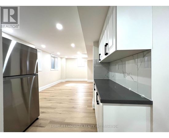 A modern kitchen with a stainless steel refrigerator and wooden flooring.