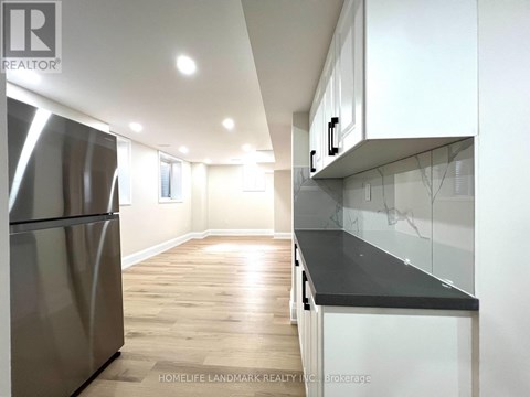 A modern kitchen with a stainless steel refrigerator and wooden flooring.